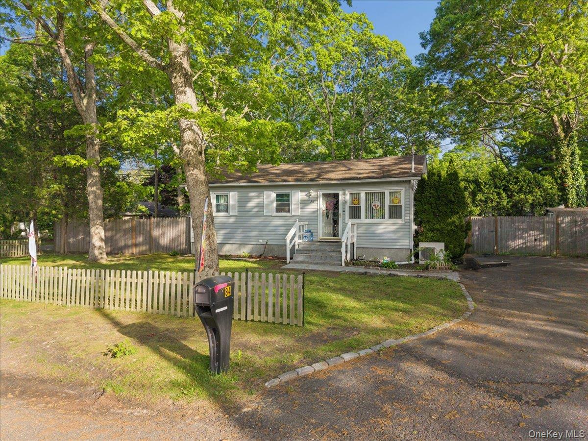 Single-story home with a white picket fence, mature trees, and a driveway.