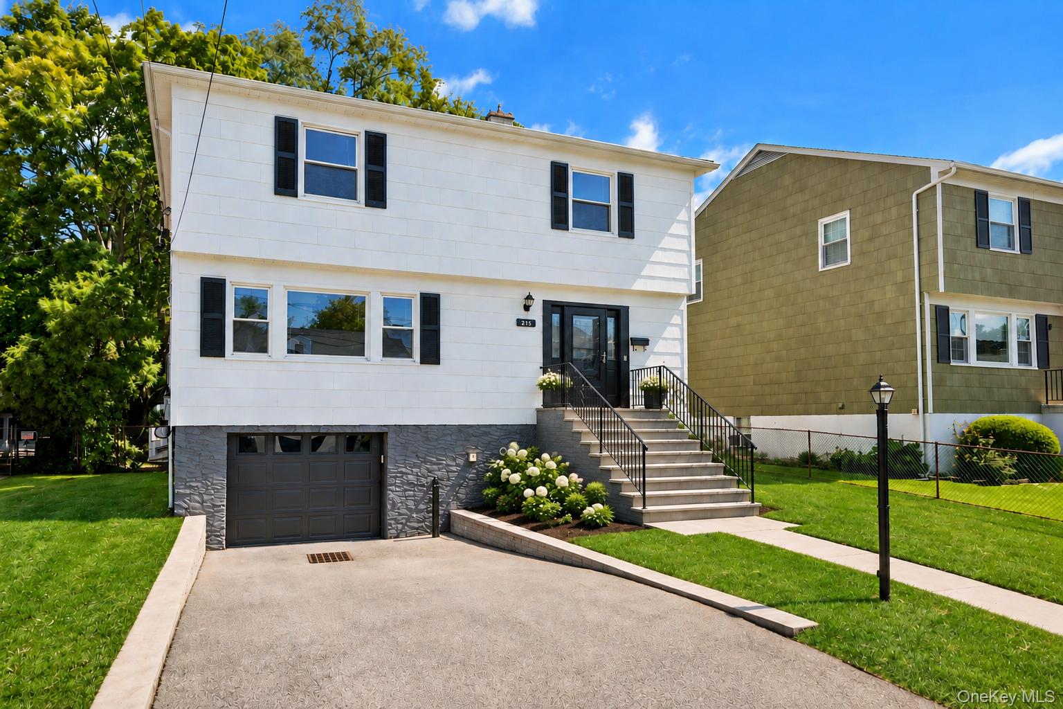 White two-story house with black shutters, stone-faced lower level, attached garage, and front steps.