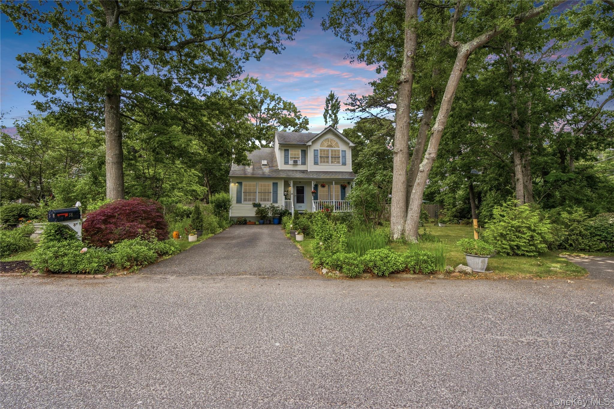 Two-story house with blue shutters, a covered porch, and a landscaped driveway beneath mature trees.