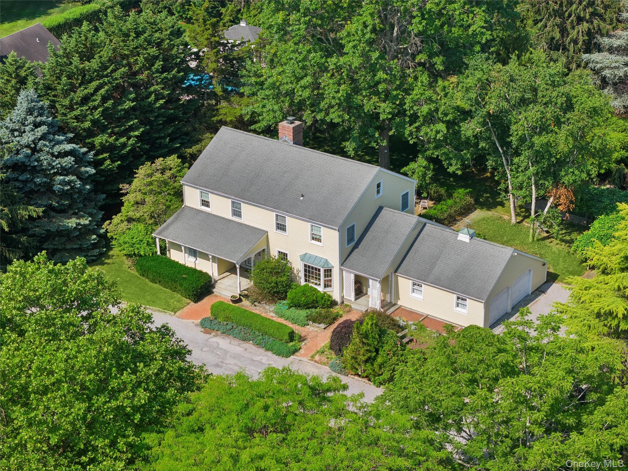 Aerial view of a two-story home with attached garage amid mature trees and landscaped grounds.