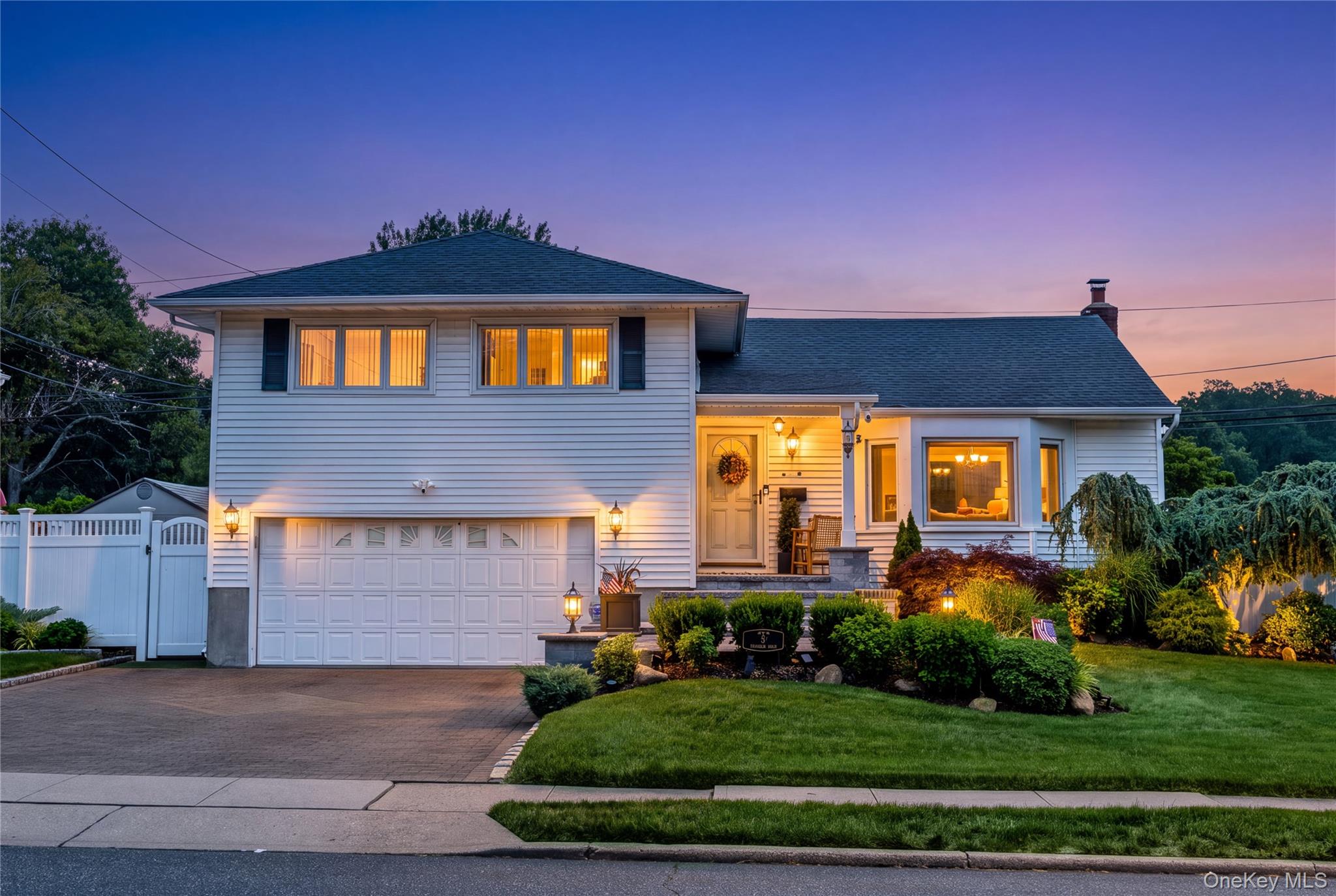 Two-story white house at dusk with a double garage, warmly lit windows, and landscaped front yard.