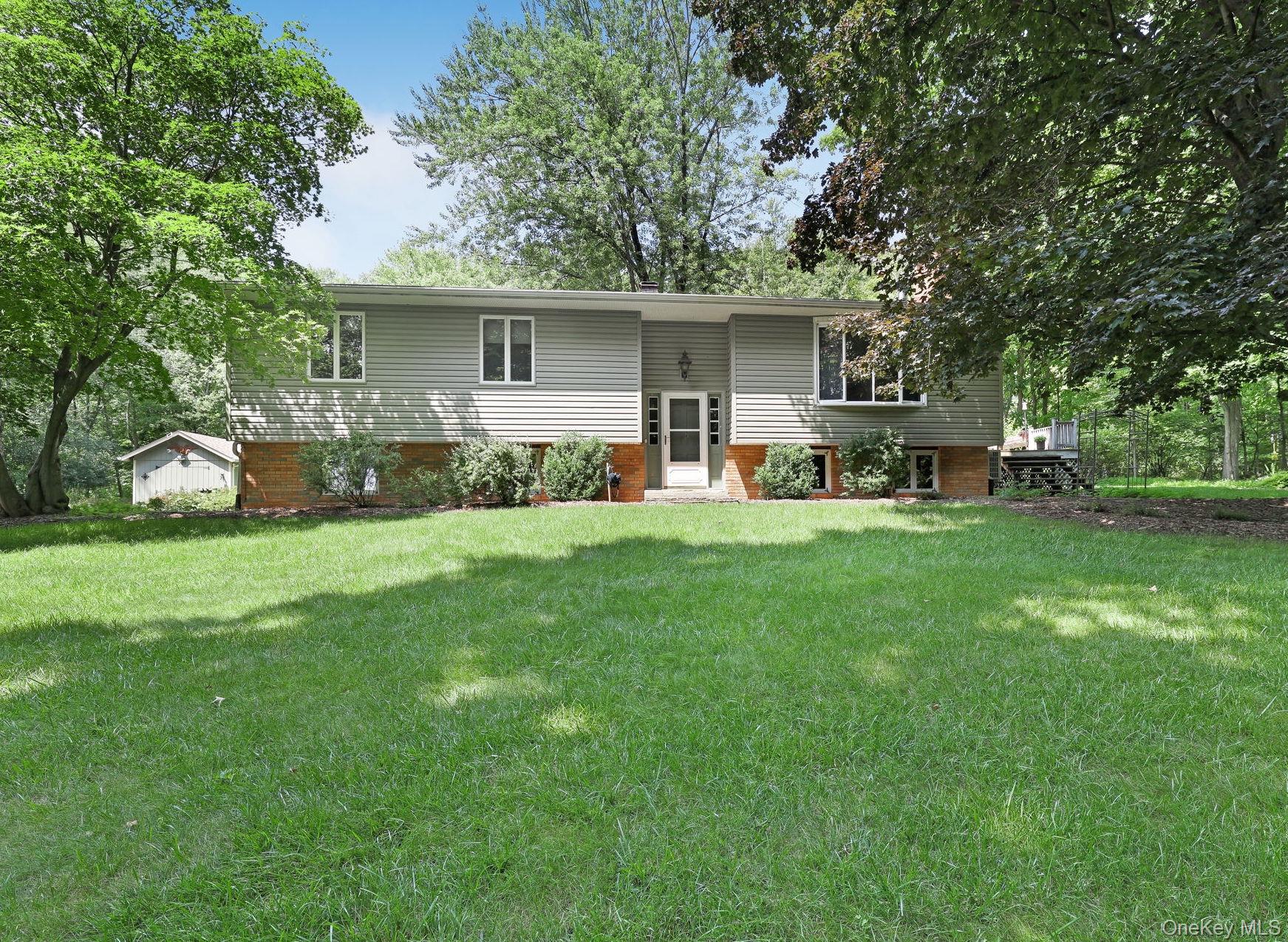 Split-level house with gray siding and brick lower facade, surrounded by mature trees and a broad lawn.