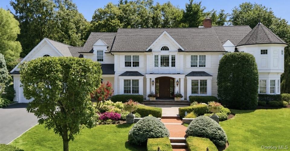 White two-story home with a turret, landscaped garden, and brick front walkway.