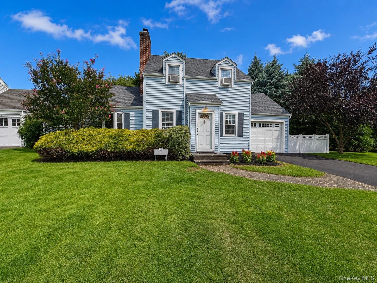Blue-gray two-story home with white trim, brick chimney, attached garage, and landscaped front lawn.