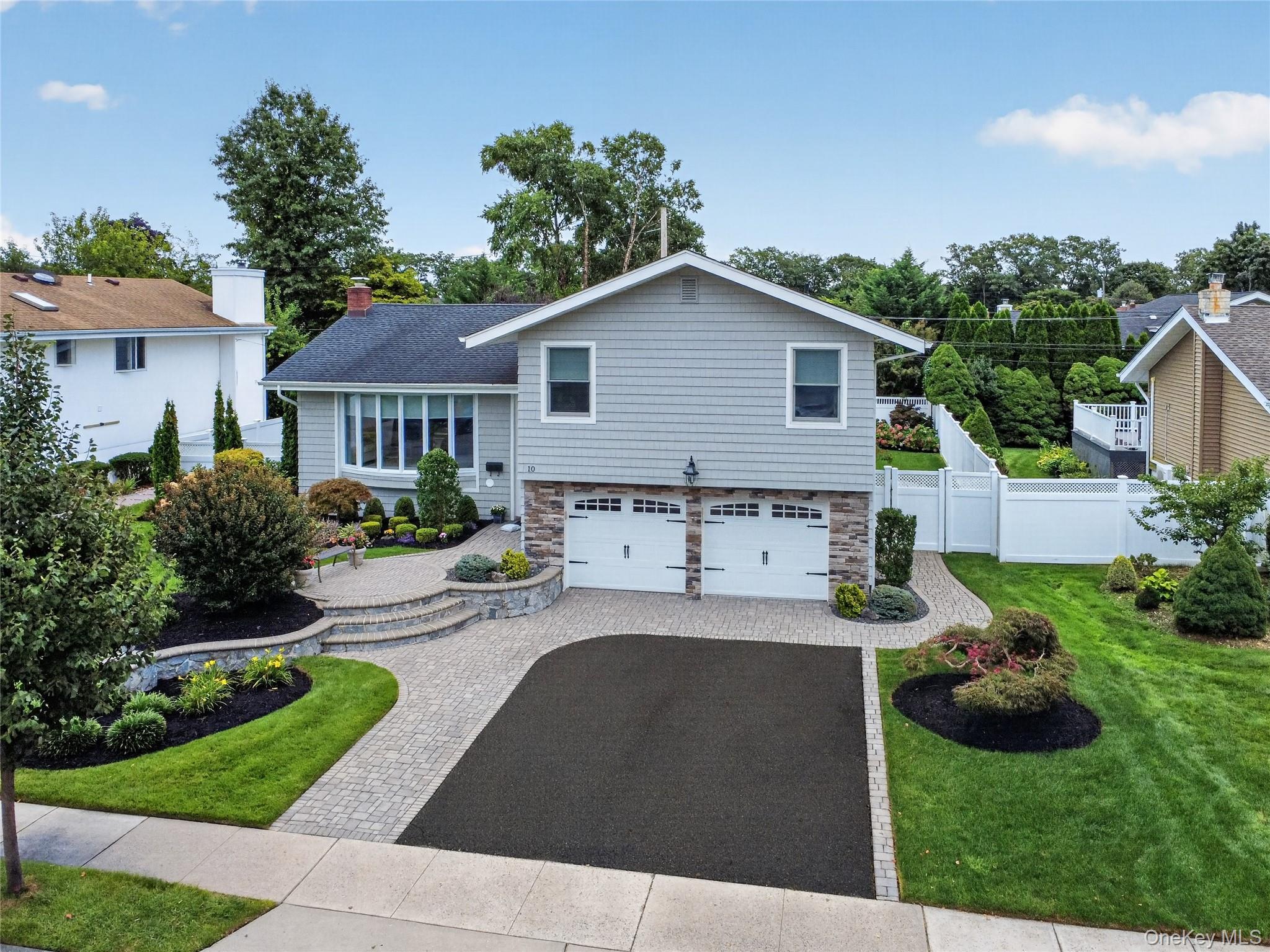 Gray shingle-style home with two garage doors, landscaped gardens, and a broad paved driveway.