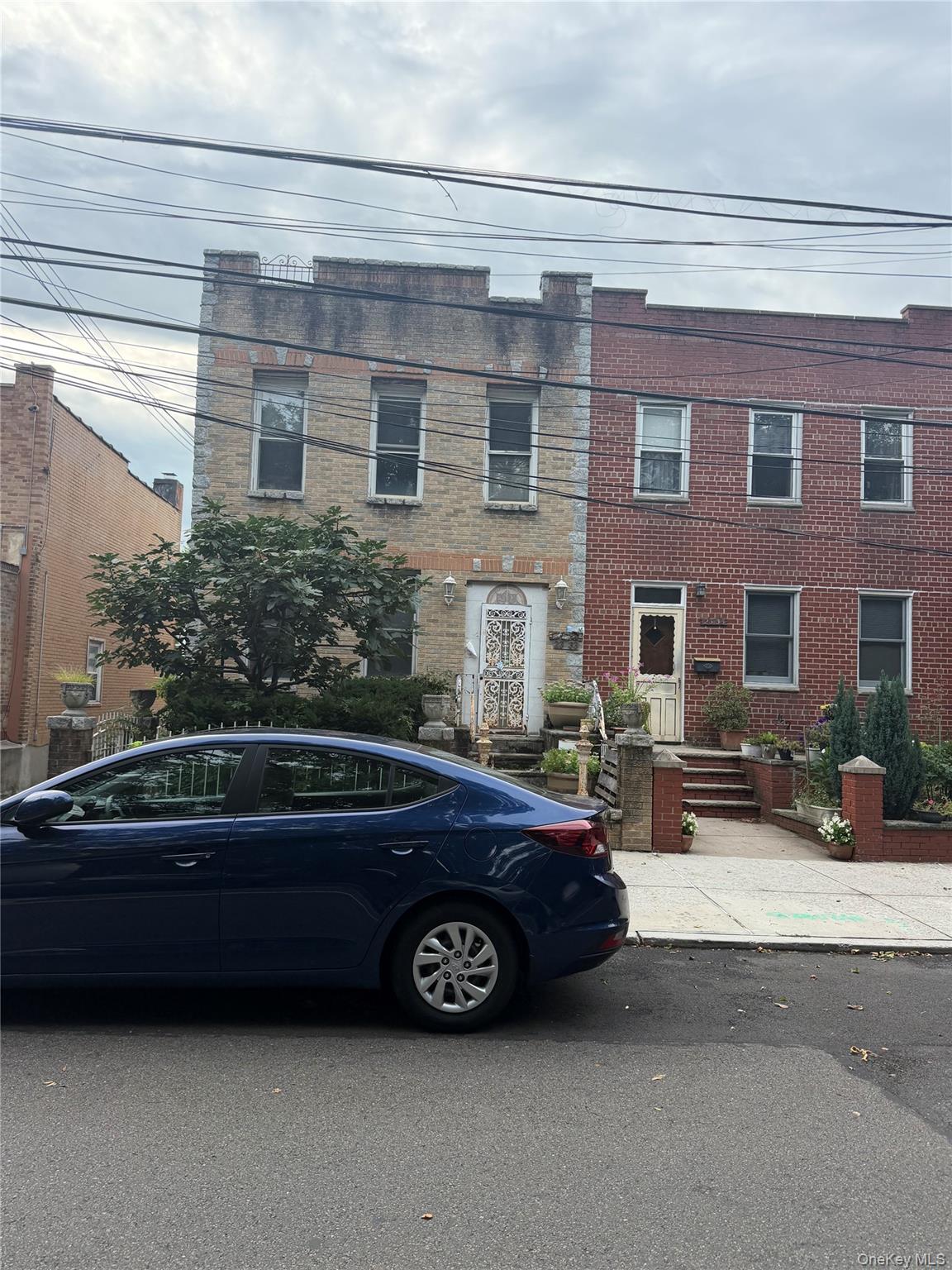 Attached brick homes with a decorative white metal entry door, front gardens, and a blue sedan parked outside.