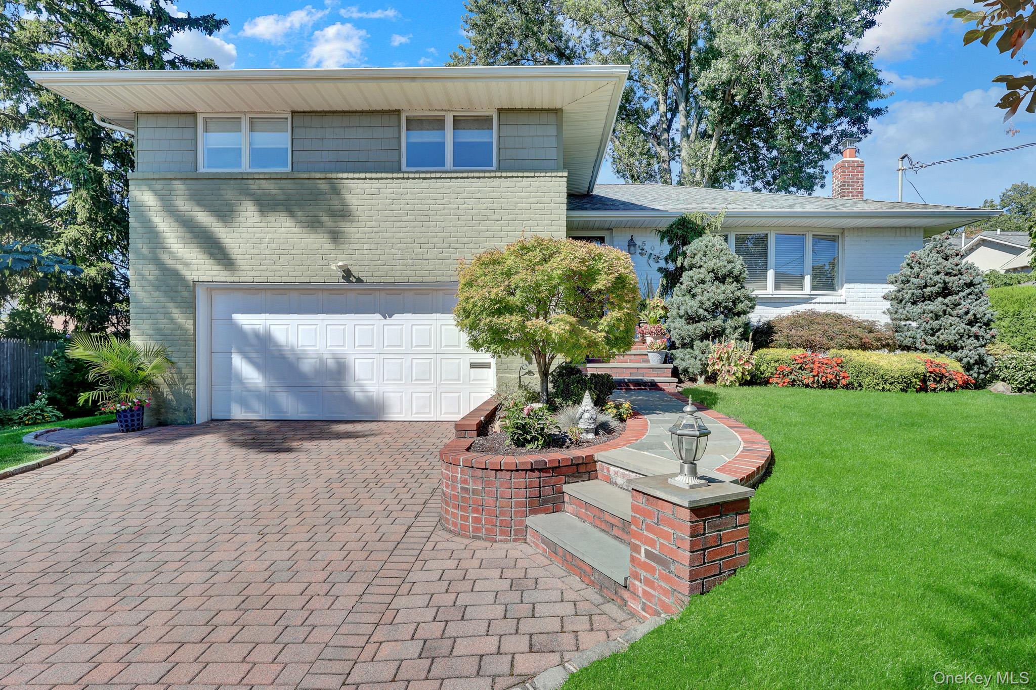 Two-story brick home with a paver driveway, curved garden walls, and landscaped front lawn.