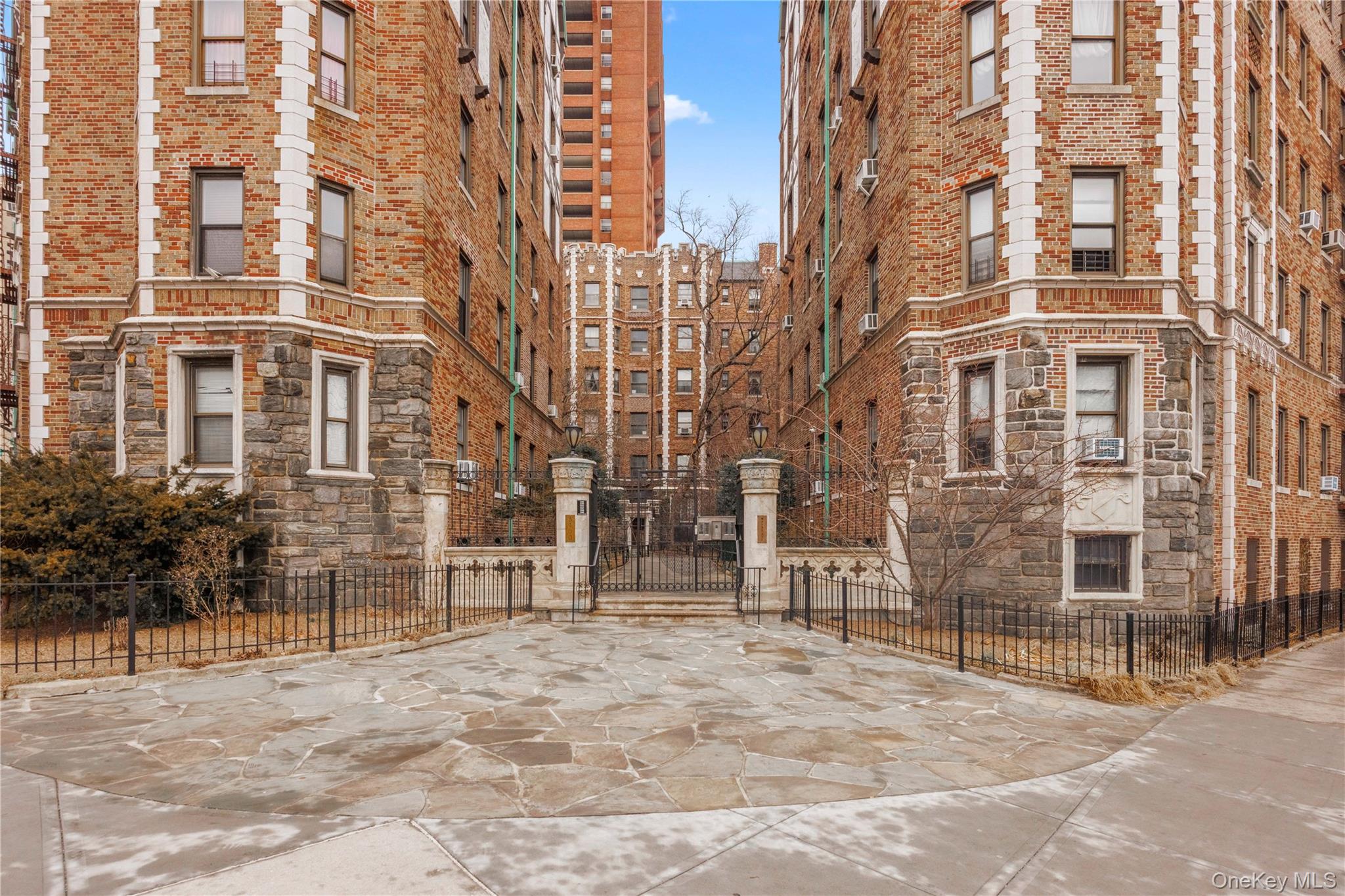 Paved courtyard between red-brick apartment buildings, with stone bases and a gated entrance.