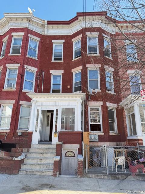 Red-brick attached homes with bay windows, stone stoops, and a chain-link fence along the sidewalk.