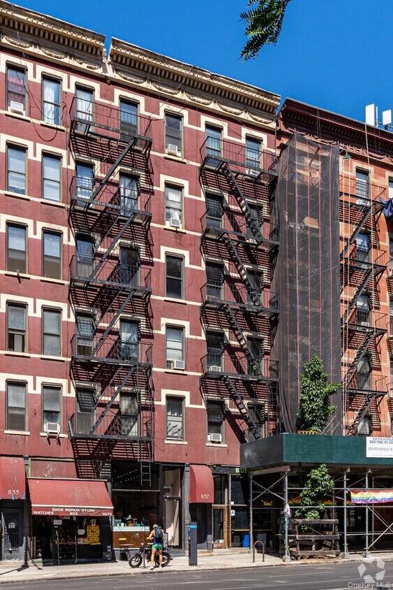 Red-brick Manhattan buildings with black fire escapes and scaffolding beside ground-floor storefronts.