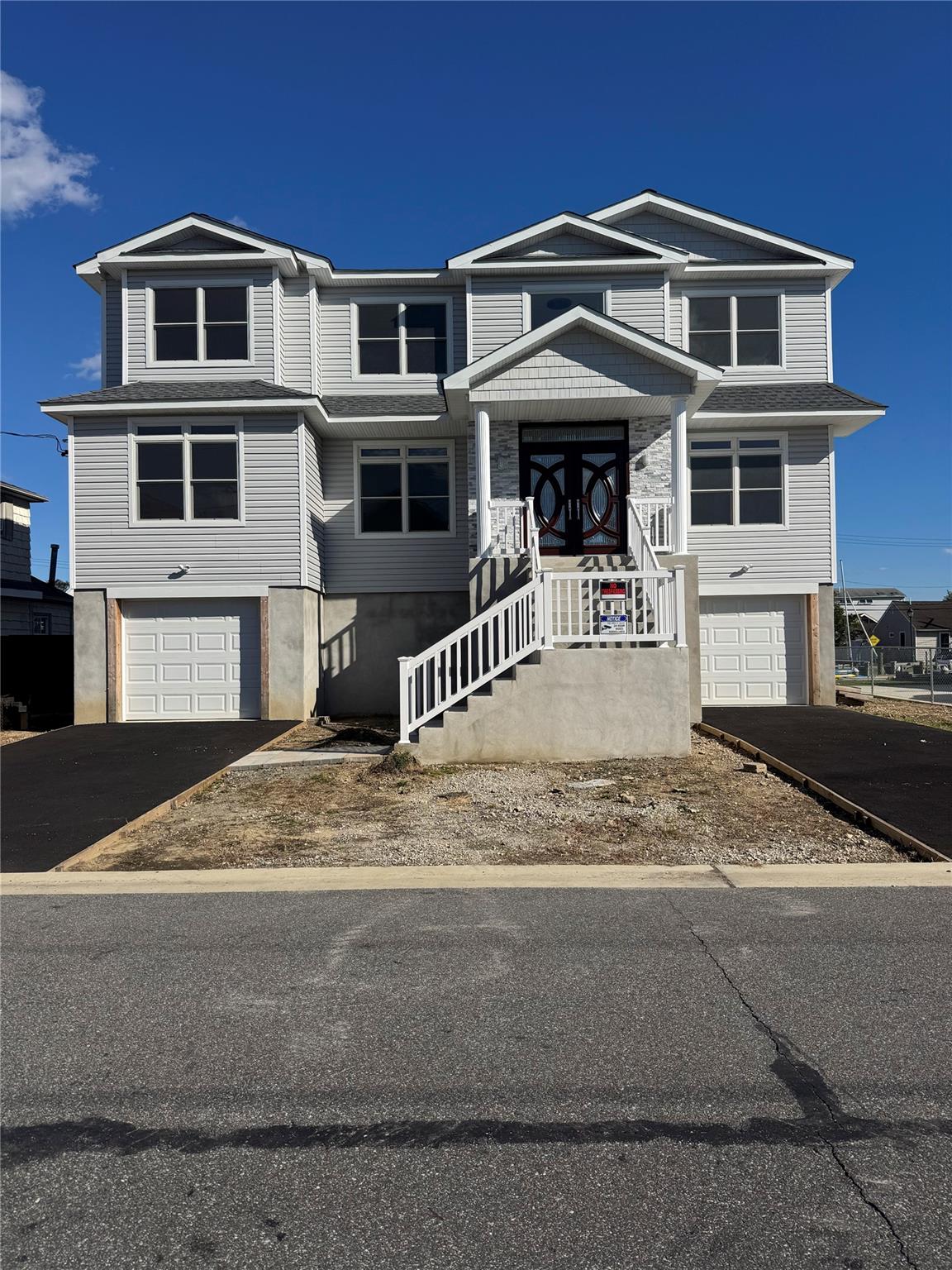Two-story gray-sided house with a stone-accented entrance, raised stairs, and two garage doors.