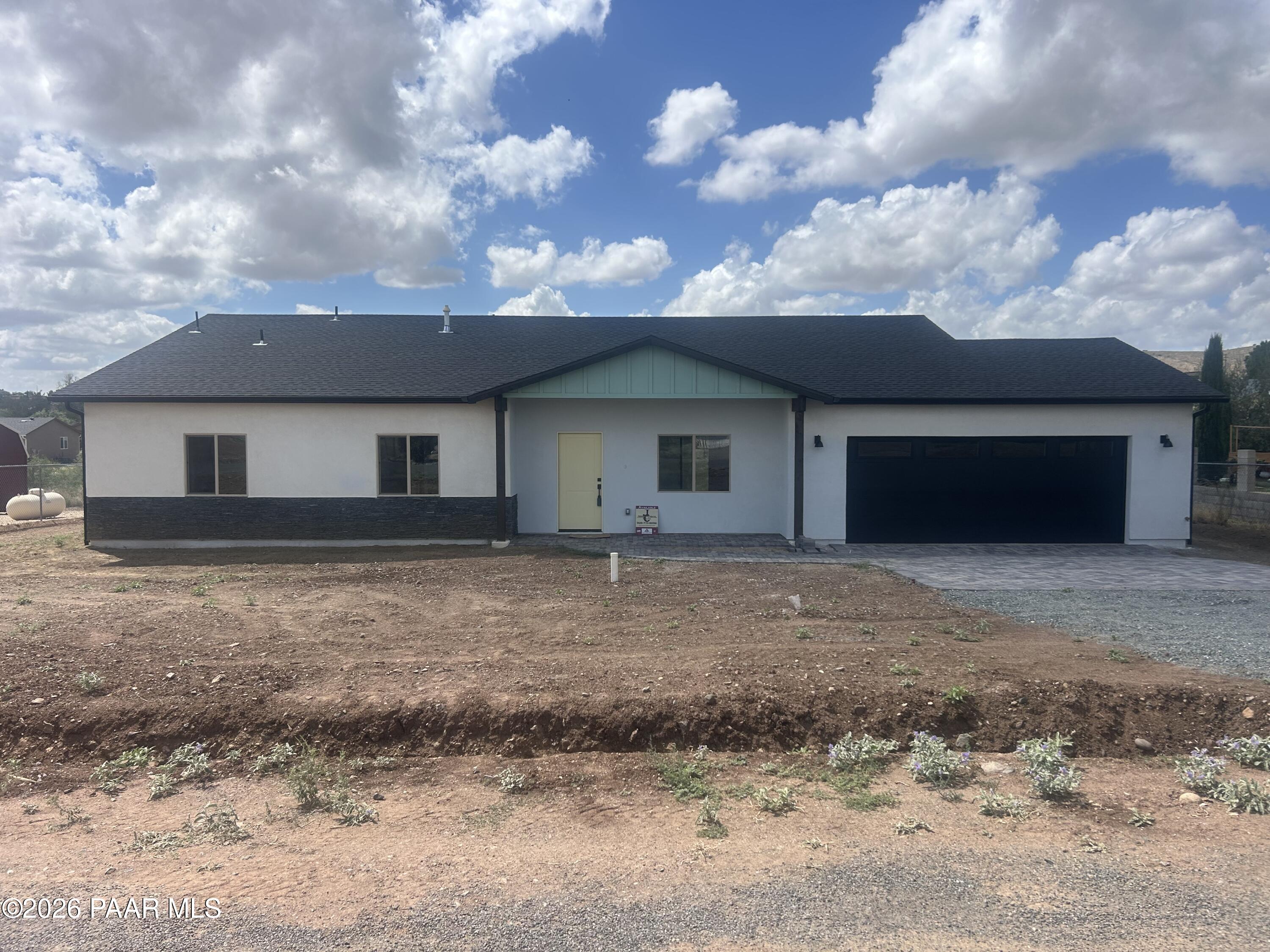 Single-story home with a dark roof and two-car garage on a mostly bare lot.