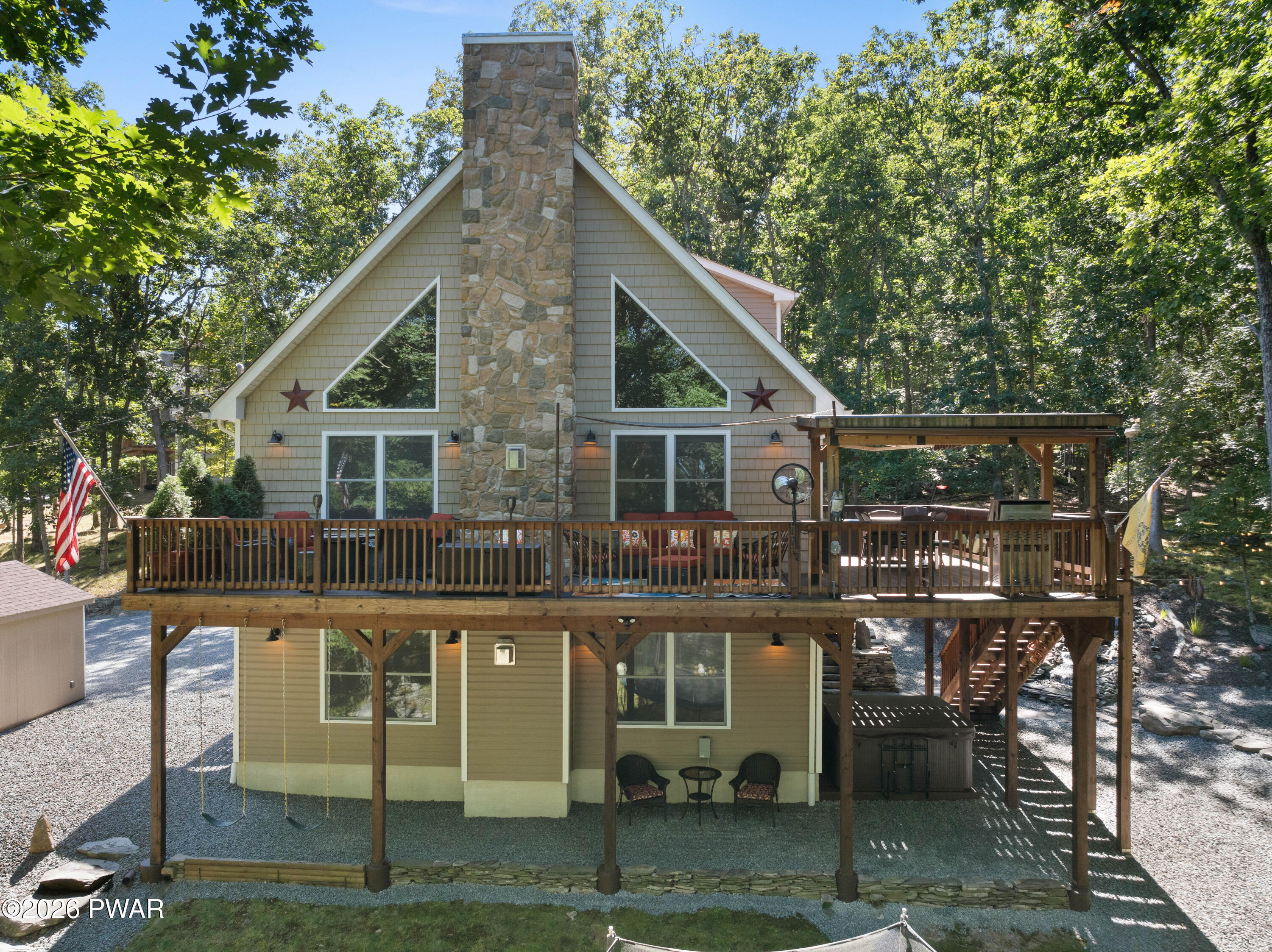 Wooded A-frame home with a stone chimney, large elevated deck, and swings beneath it.