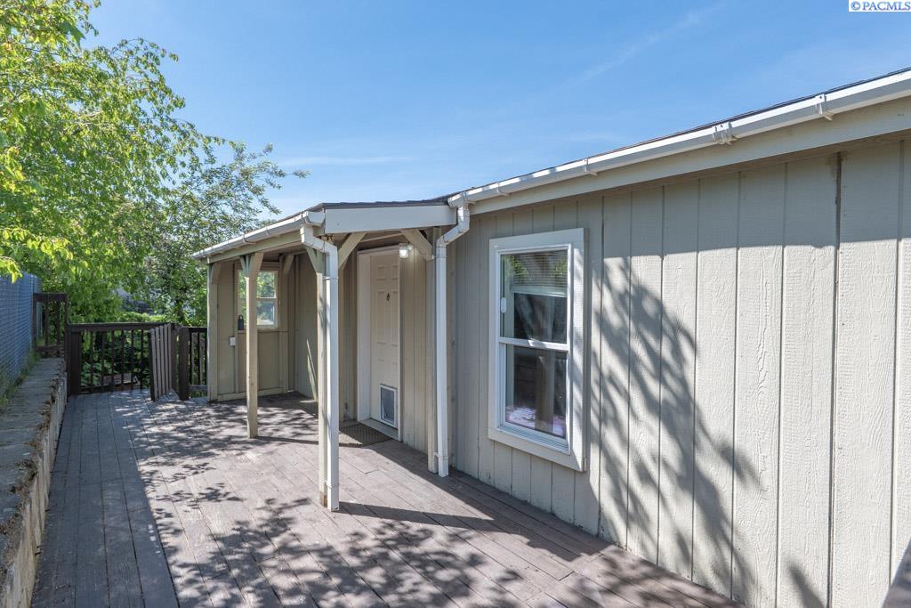 House exterior with a long wooden deck and covered entrance beneath leafy trees.