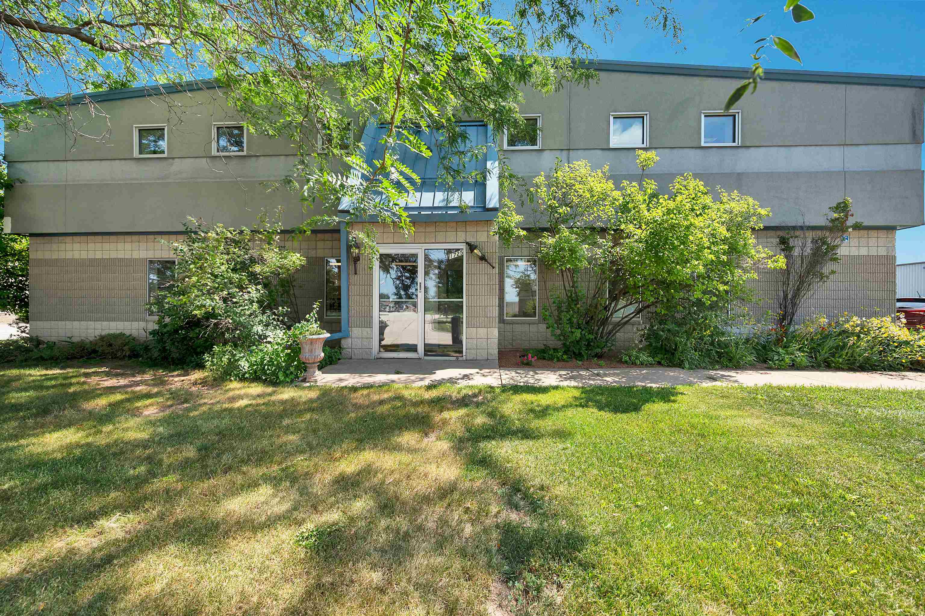Two-story building with a glass entrance, landscaped shrubs, and a broad green lawn.
