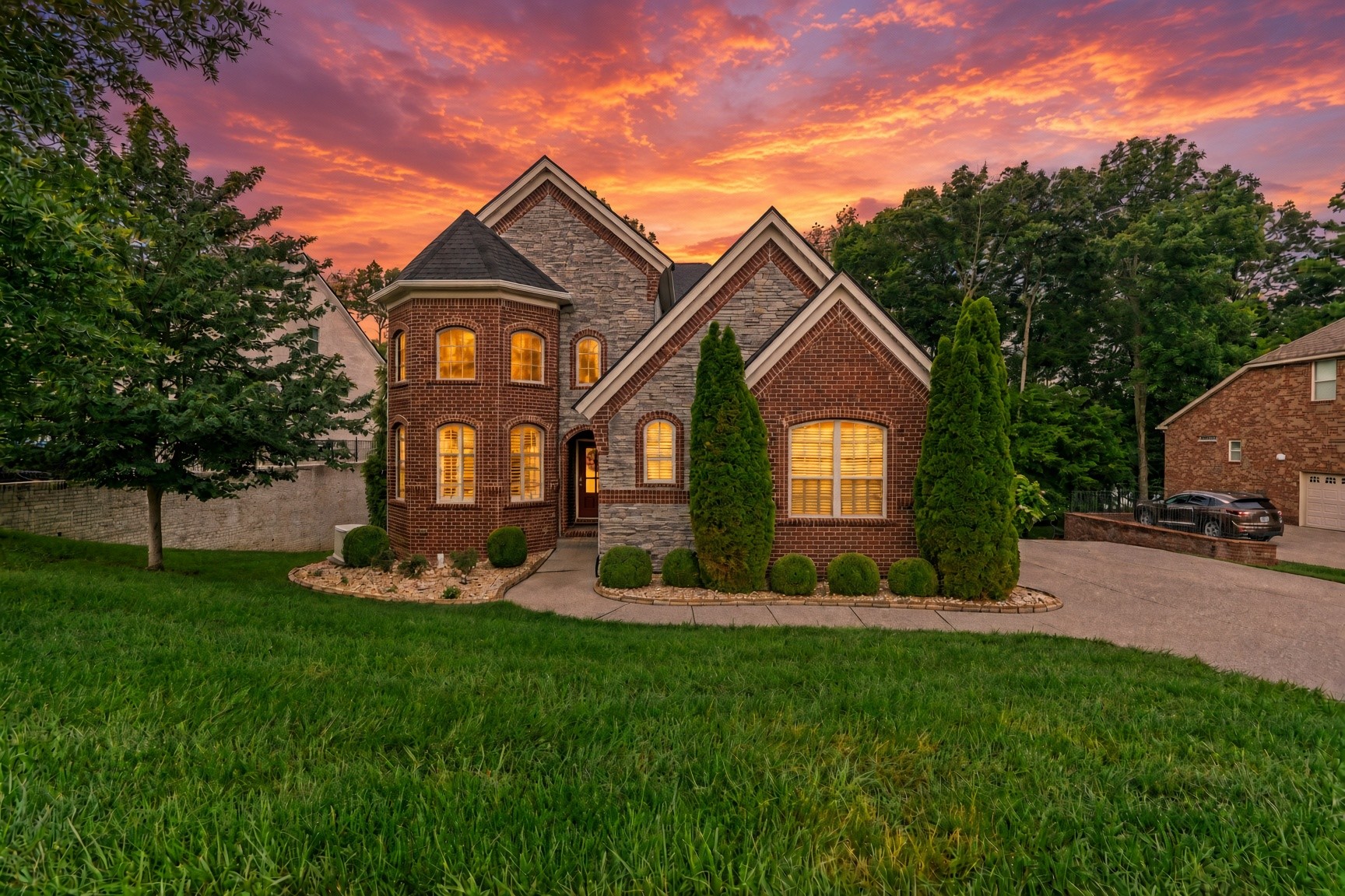 Brick and stone home with illuminated windows and landscaped grounds beneath a vivid sunset sky.