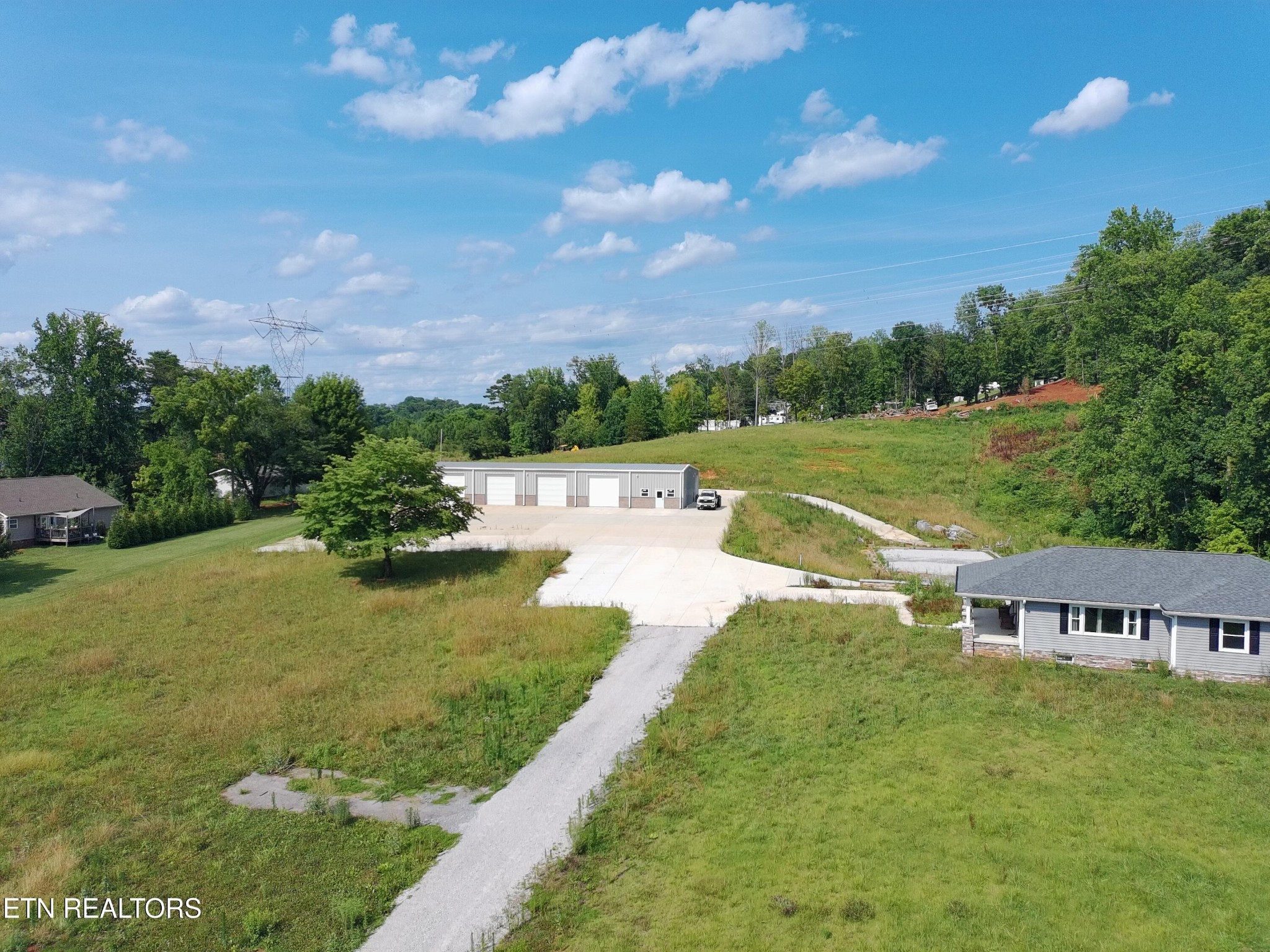 Aerial view of a grassy property with a multi-bay garage and long paved driveway.