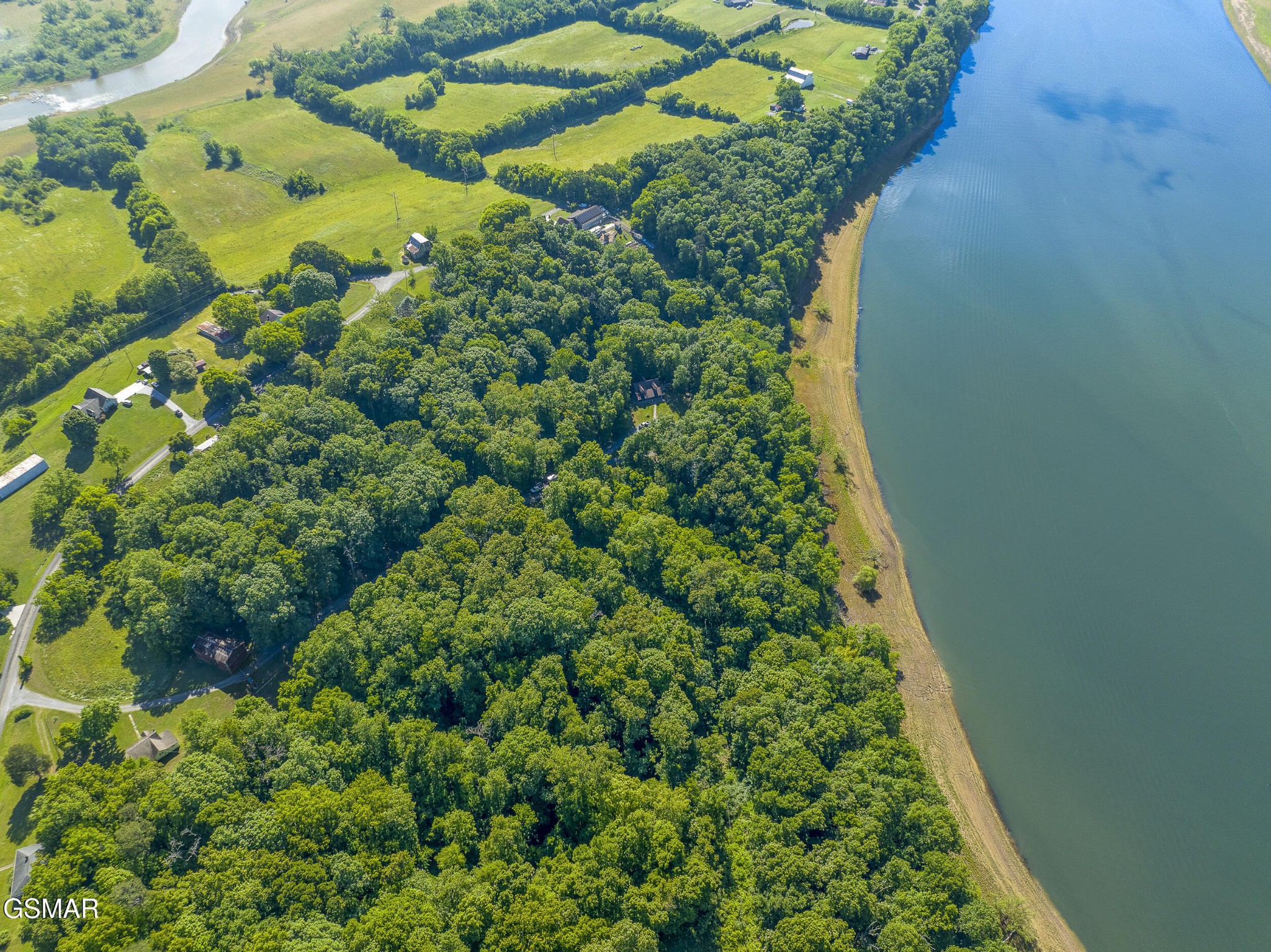 Aerial view of wooded homes and open fields along a broad river.