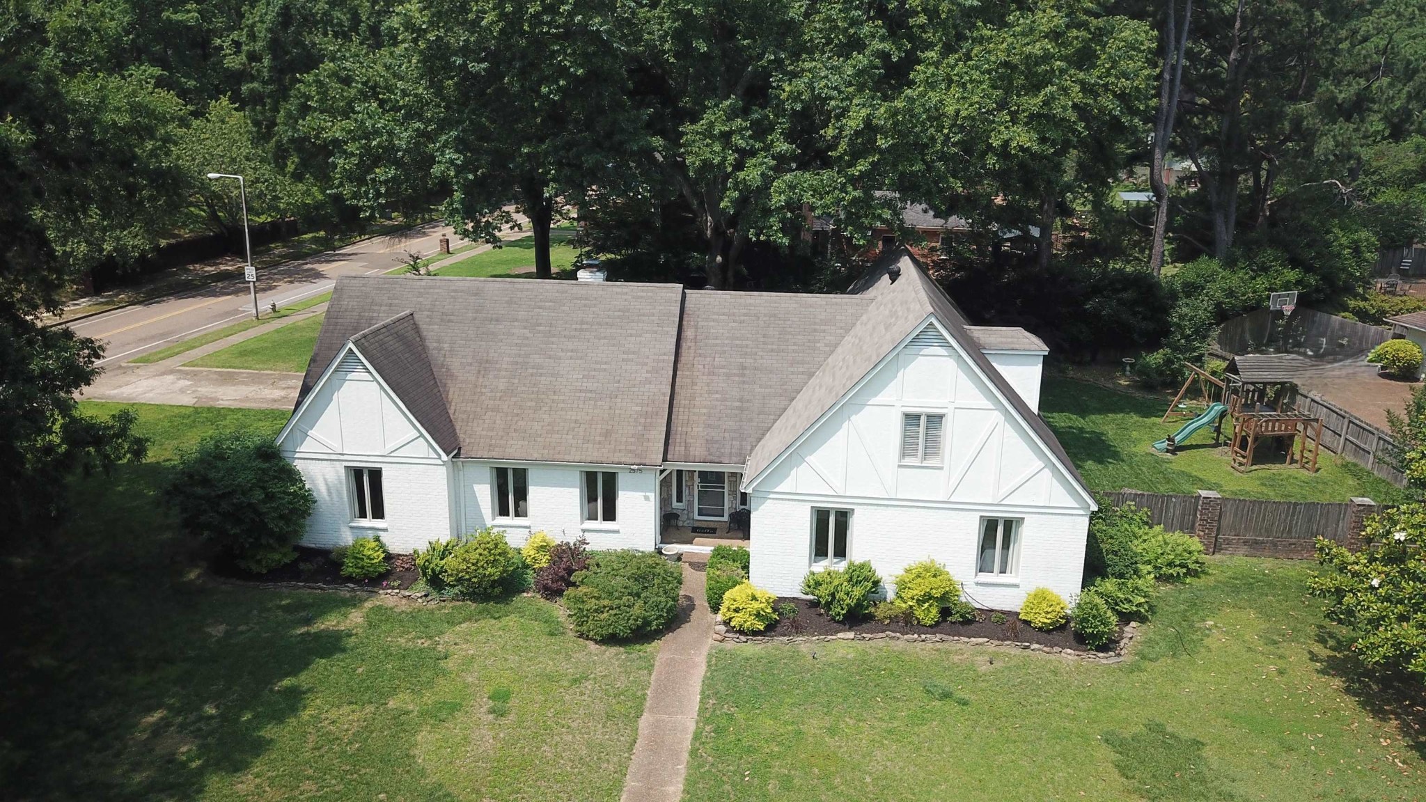 Aerial view of a white gabled house with landscaped gardens and a fenced backyard playset.