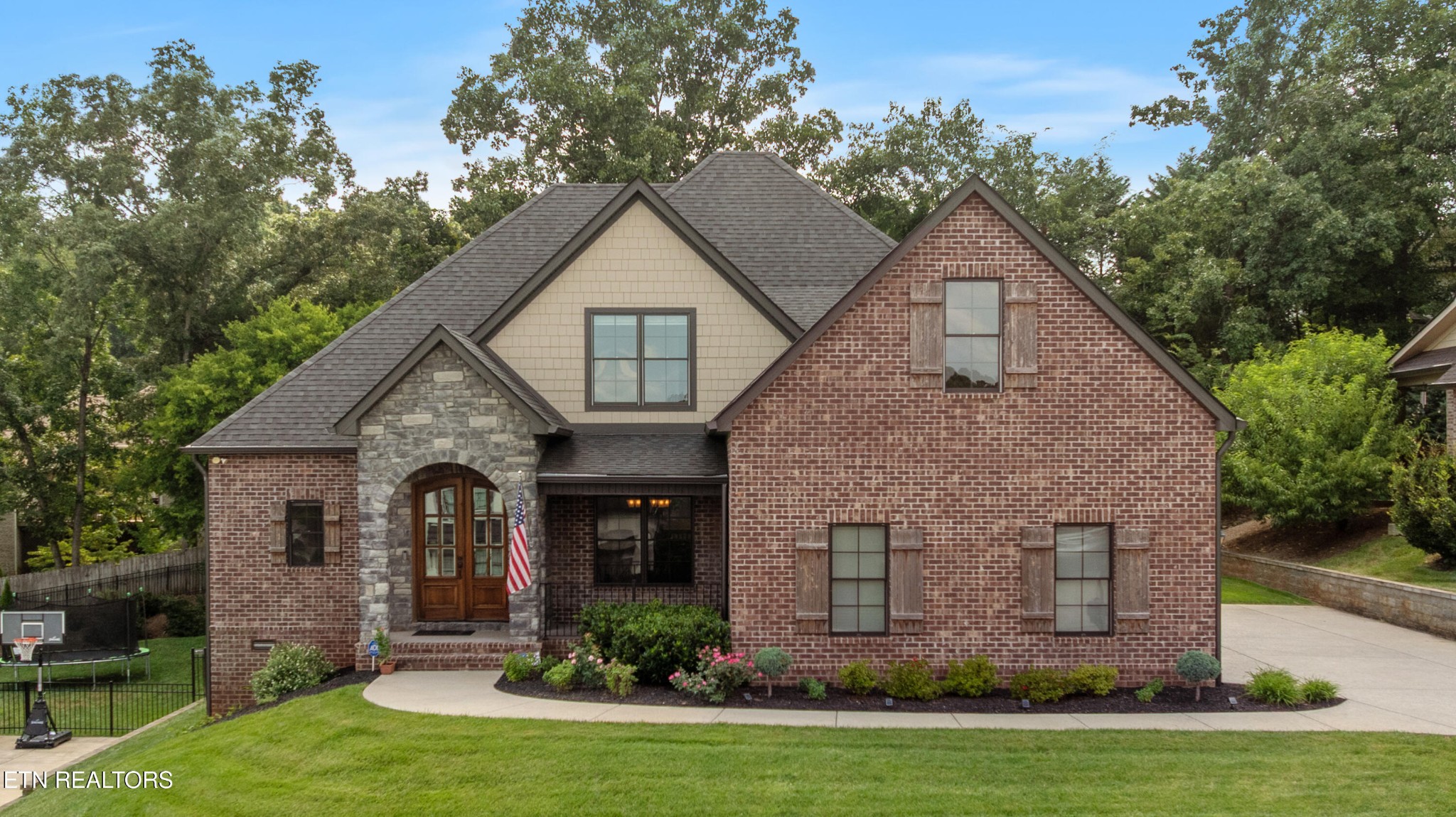 Two-story brick home with a stone-arched entrance, steep gables, and landscaped front yard.