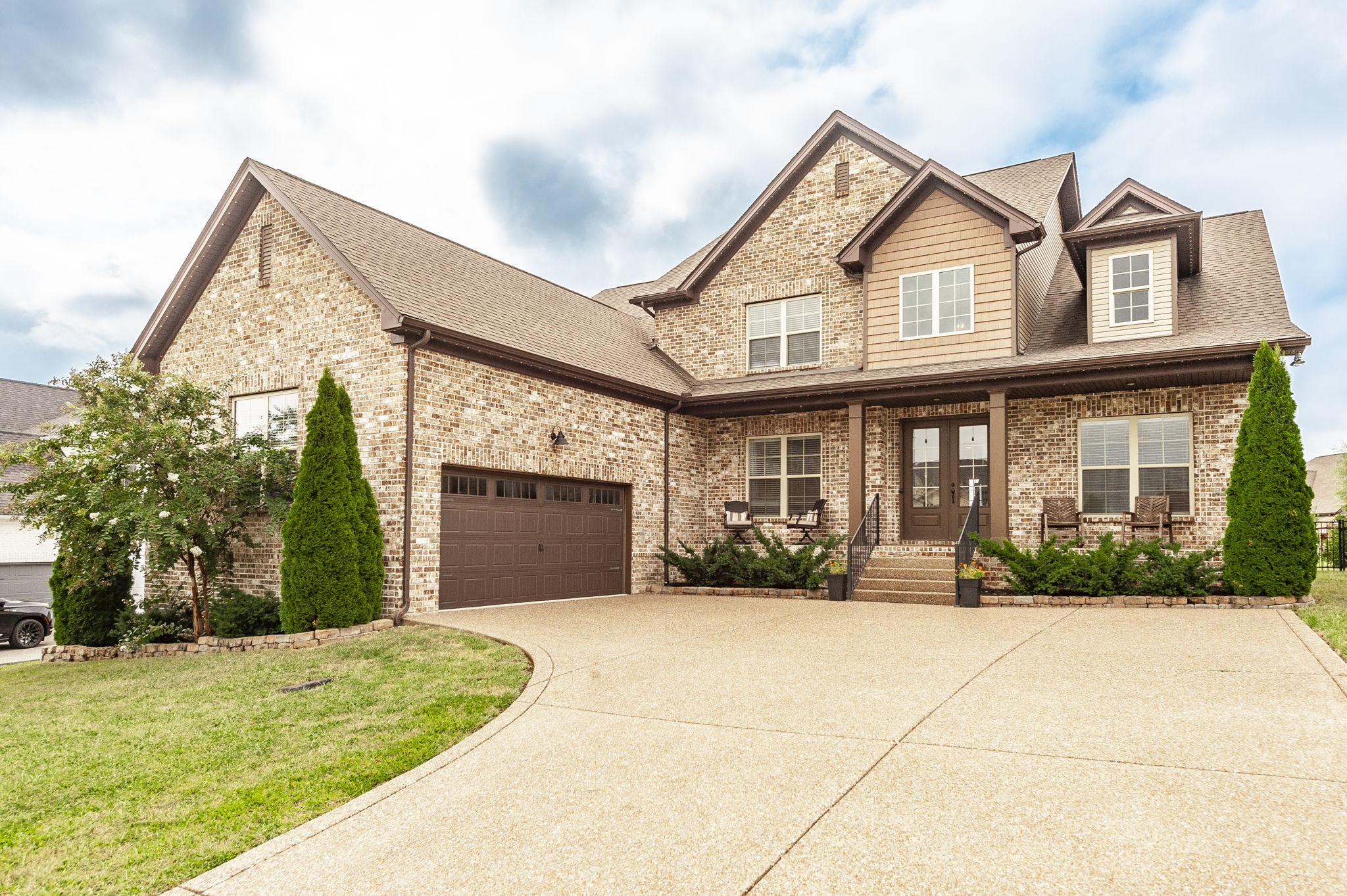Two-story brick house with a broad driveway, attached garage, and covered porch.