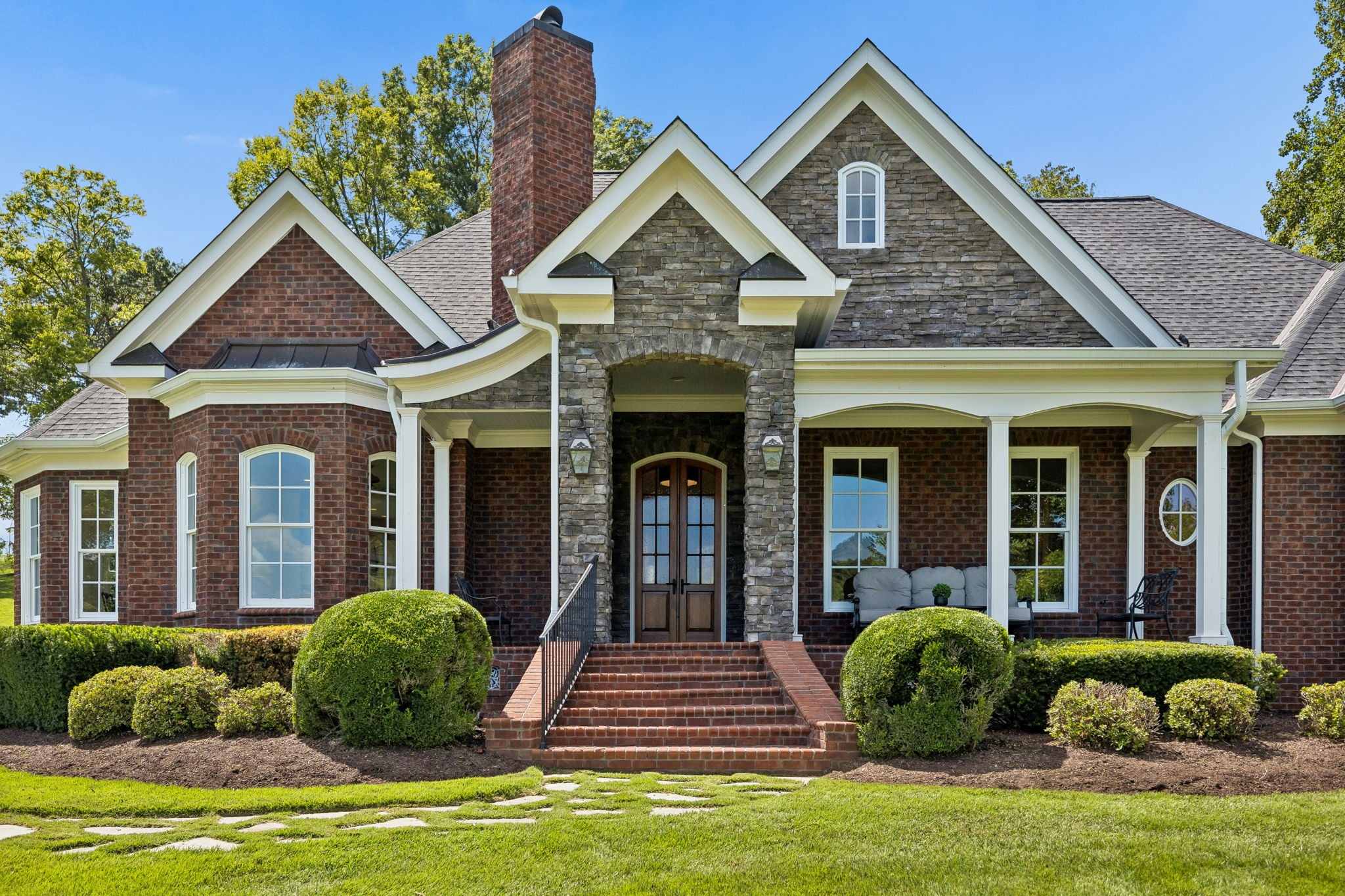 Brick and stone home with multiple gables, a covered porch, and landscaped front lawn.