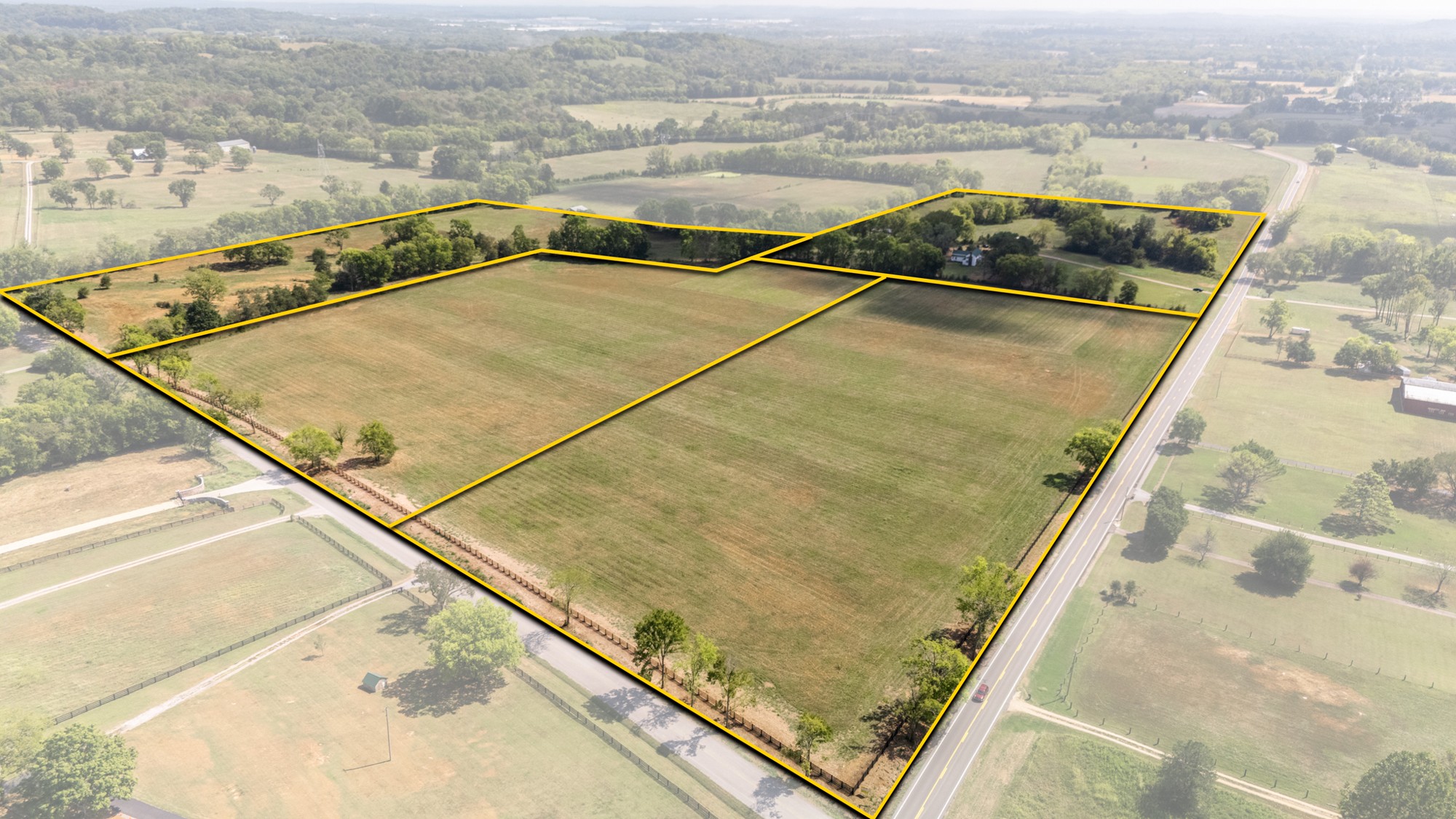 Aerial view of rural fields and parcels outlined in yellow beside a paved highway.