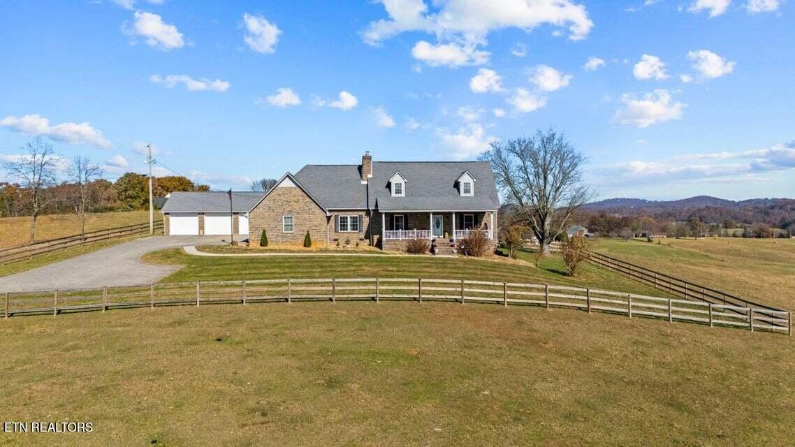 Stone-and-brick country home with an attached garage, fenced lawn, and rolling countryside.