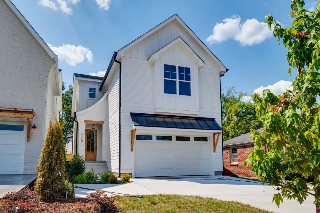 Two-story white house with a double garage, broad driveway, and leafy trees.