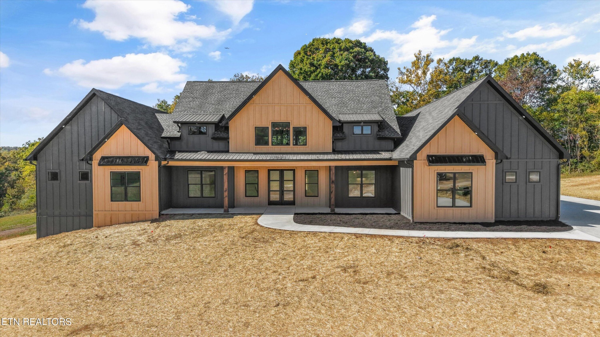 Modern farmhouse-style home with wood siding, a broad lawn, and autumn trees.