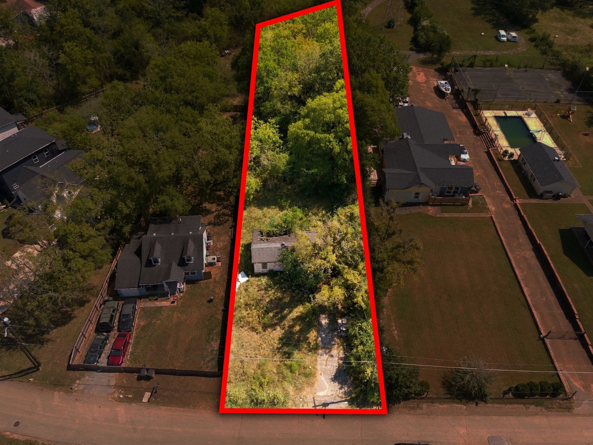 Aerial view of a tree-covered residential lot outlined in red, with a small house and driveway.