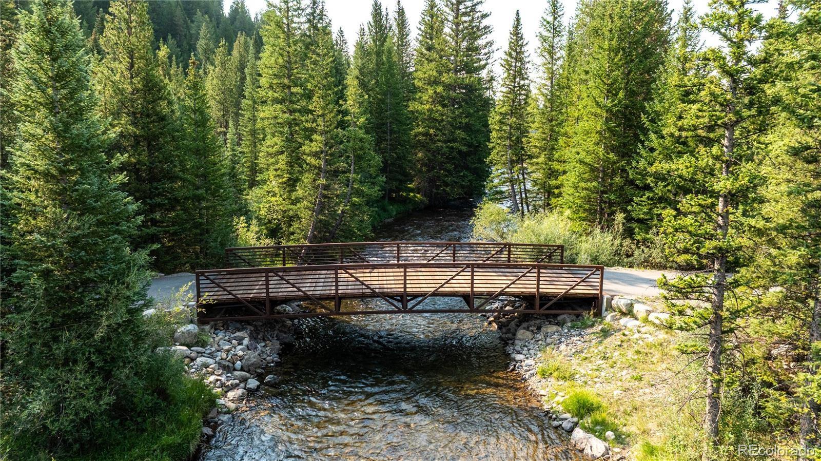 A wooden pedestrian bridge crosses a rocky stream through dense evergreen forest.