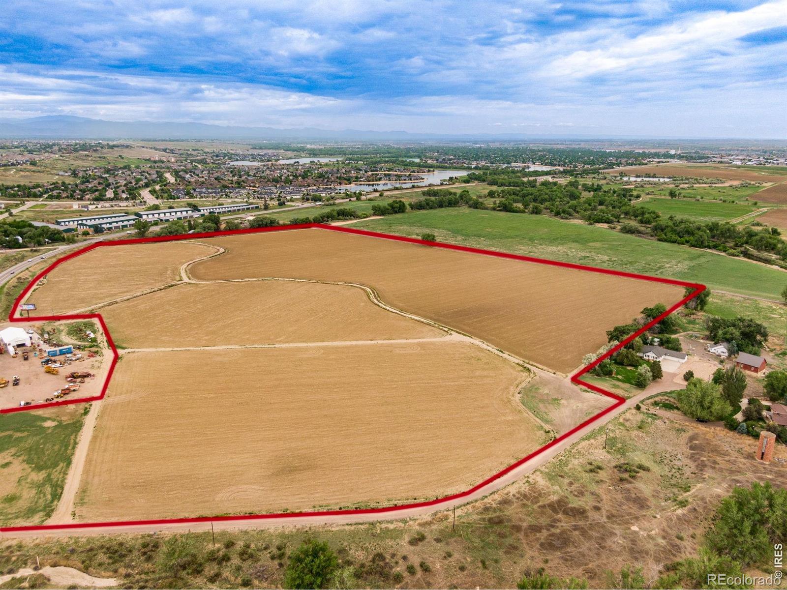 Aerial view of a large cleared land parcel outlined in red, with a neighborhood and distant mountains beyond.