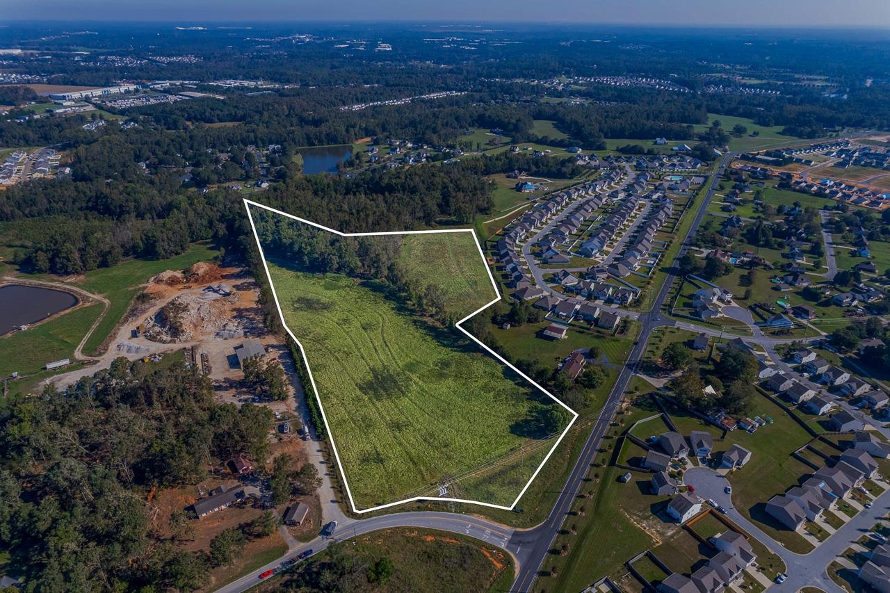 Aerial view of vacant land outlined beside a road and residential subdivision.
