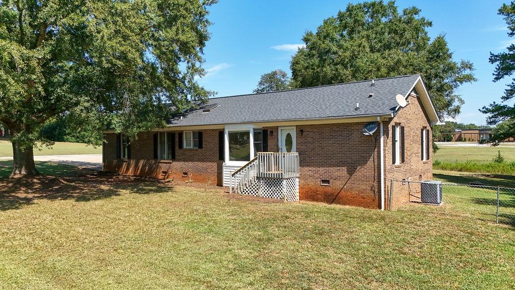 Single-story brick ranch with a white-railed porch, broad lawn, and mature trees.