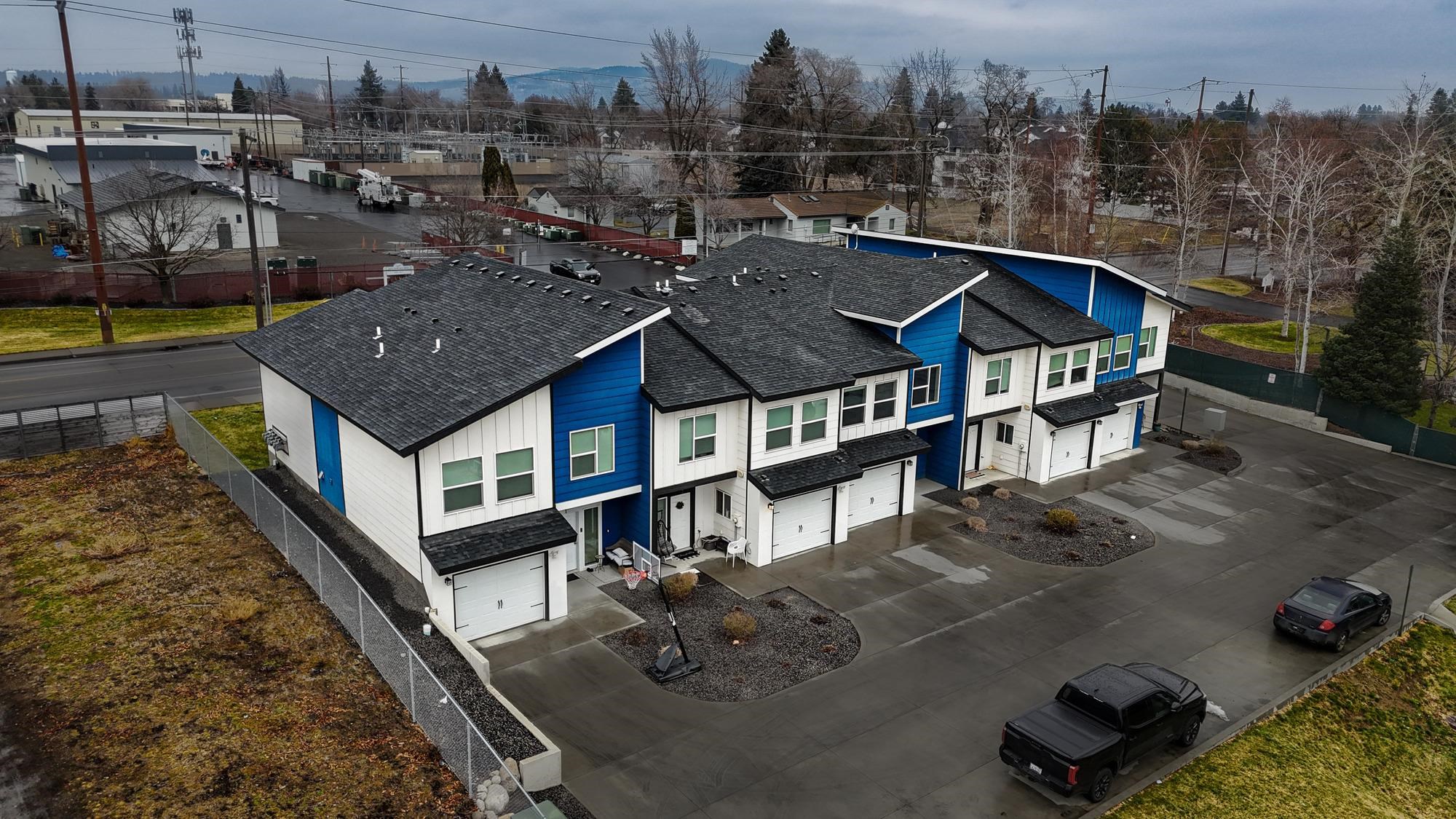 Blue-and-white townhomes with private garages and a shared paved parking area, seen from above.