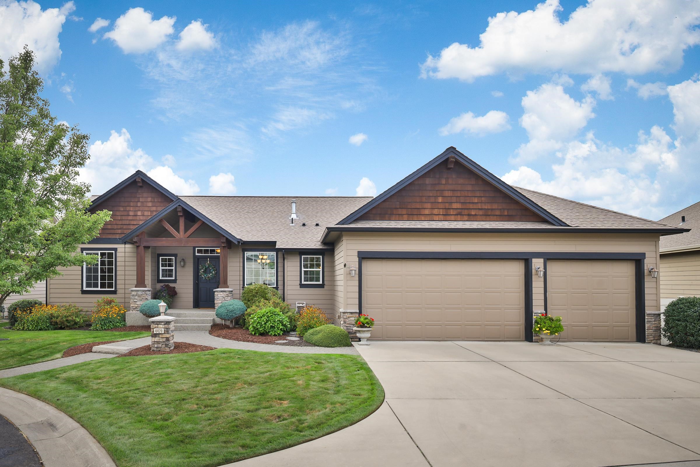 Single-story home with a double garage, covered entry, landscaped flower beds, and curved front lawn.