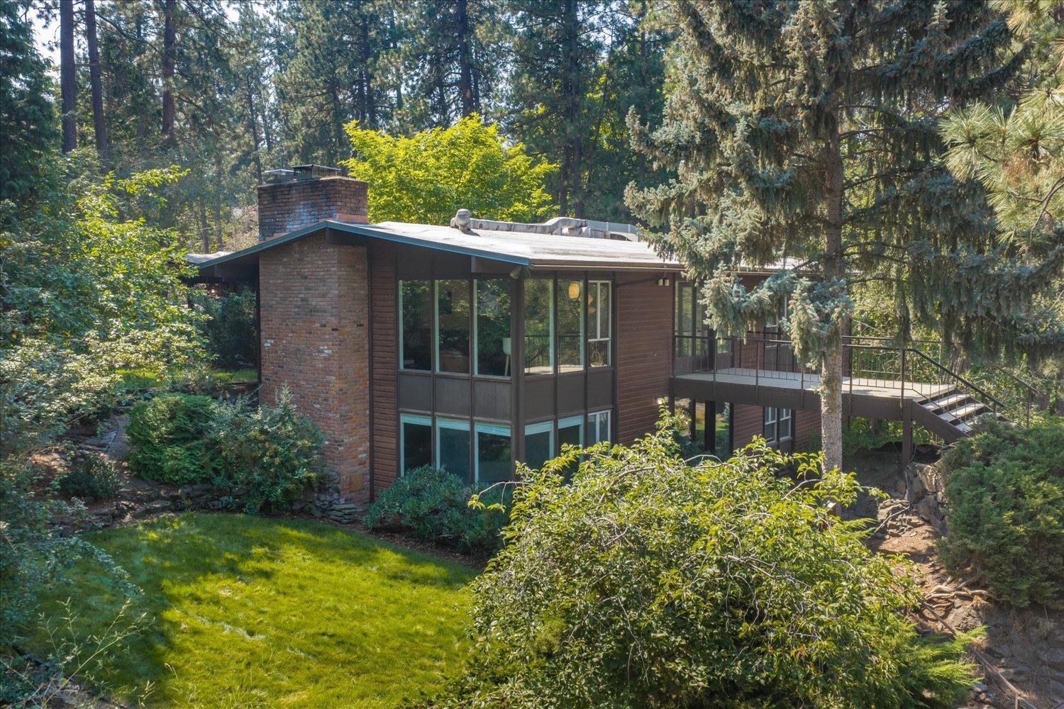 Modern two-story home nestled among mature evergreens, with a brick chimney and elevated deck.