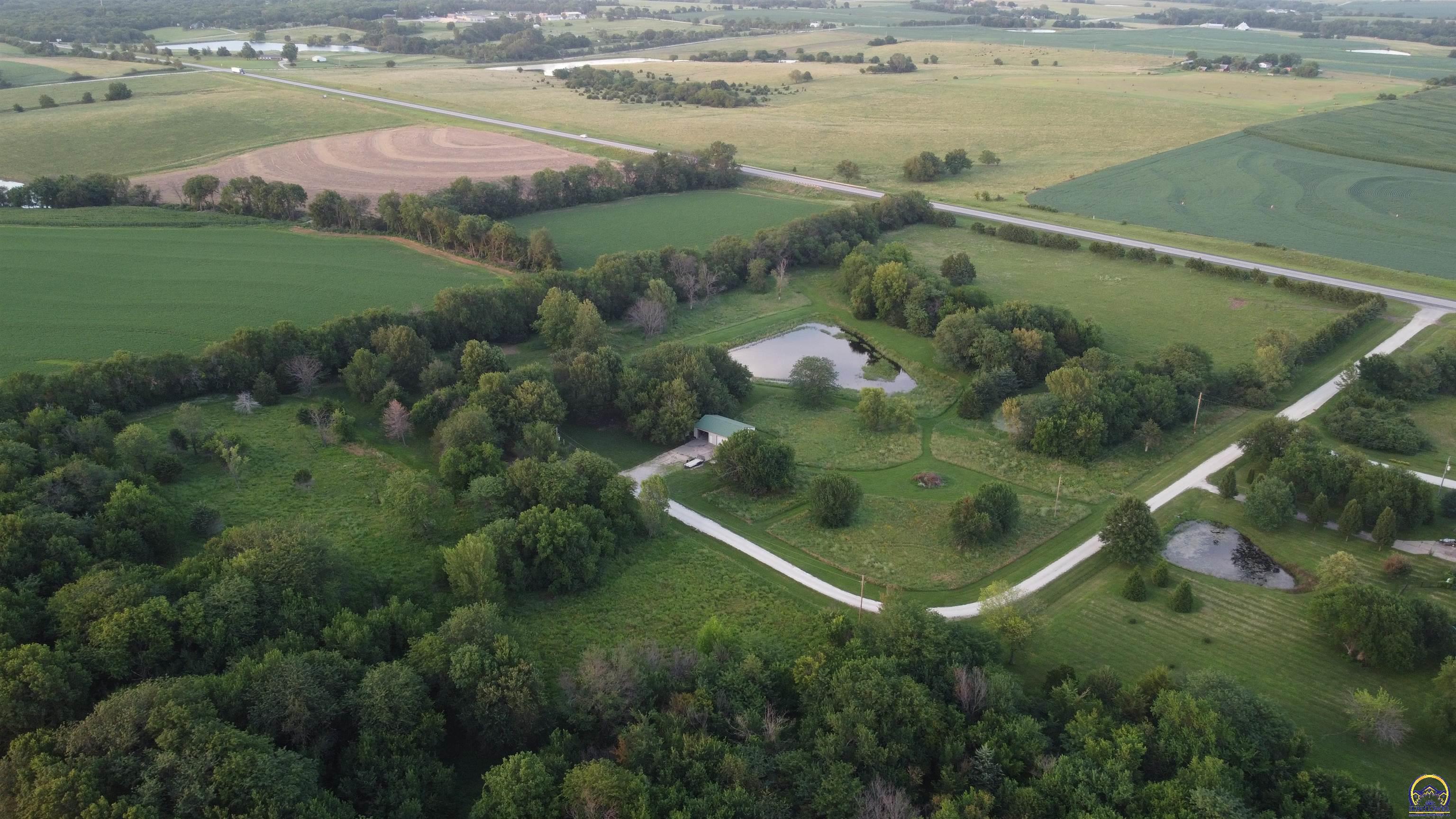 Aerial view of green rural land with fields, tree-lined roads, two ponds, and an outbuilding.