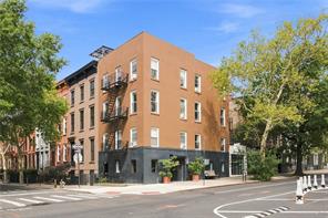 Red-brick corner apartment building with black fire escapes and leafy street trees.