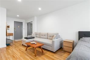 Furnished apartment living area with a gray sofa, hardwood floors, and a bed in the foreground.