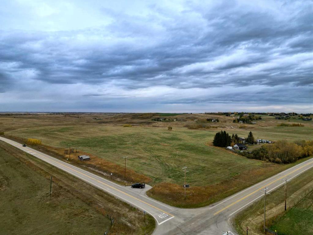 Open rural fields and scattered homes beside a paved-road intersection under a cloudy sky.