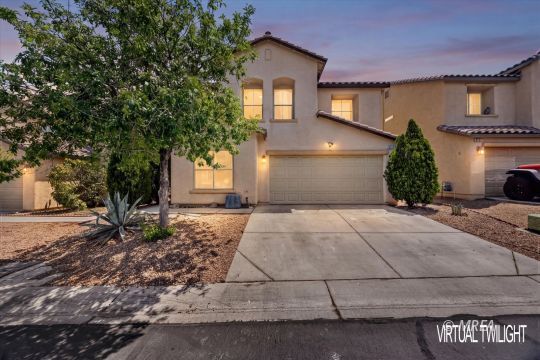 Two-story stucco home with a double garage and desert landscaping at dusk.