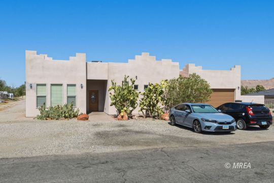Modern stucco home with stepped parapets, desert plants, and two cars parked in front.